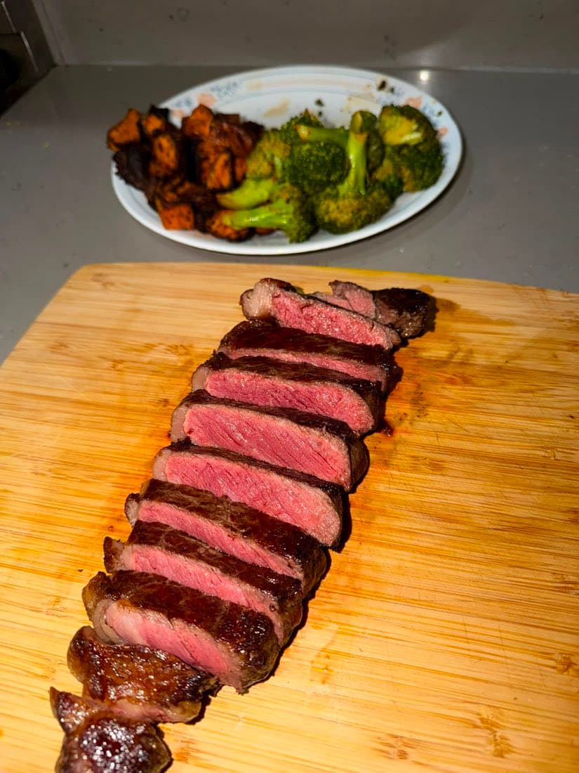 Sliced NY striploin cooked medium-rare, served with roasted sweet potato and broccoli